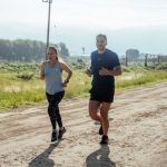 Active couple jogging on a dirt road in a scenic rural area under the bright sun.