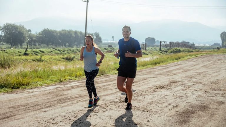 Active couple jogging on a dirt road in a scenic rural area under the bright sun.